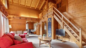 L’intérieur d’un chalet en bois, avec un canapé rouge, un téléviseur et un escalier.
