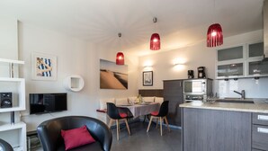 Une cuisine moderne avec un coin repas, un fauteuil en cuir noir et une suspension rouge.