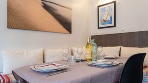 Une table à manger dressée avec des assiettes, des verres et une bouteille de vin, et sur le mur, un tableau et une photographie encadrée.