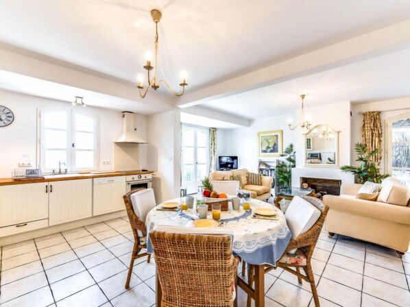 A spacious living area with a dining table, wicker chairs, a sofa, and a television.