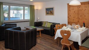 Ein möbliertes Wohnzimmer mit einer Couch, Sesseln, einem Esstisch, der für eine Mahlzeit gedeckt ist, und einem Bild an der Wand.