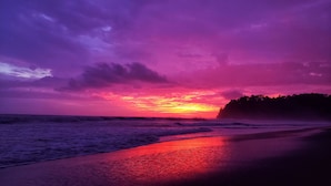 A beach at sunset with waves and a forested hill in the background. - Saltish Hotel & Villas (Bahía Ballena)