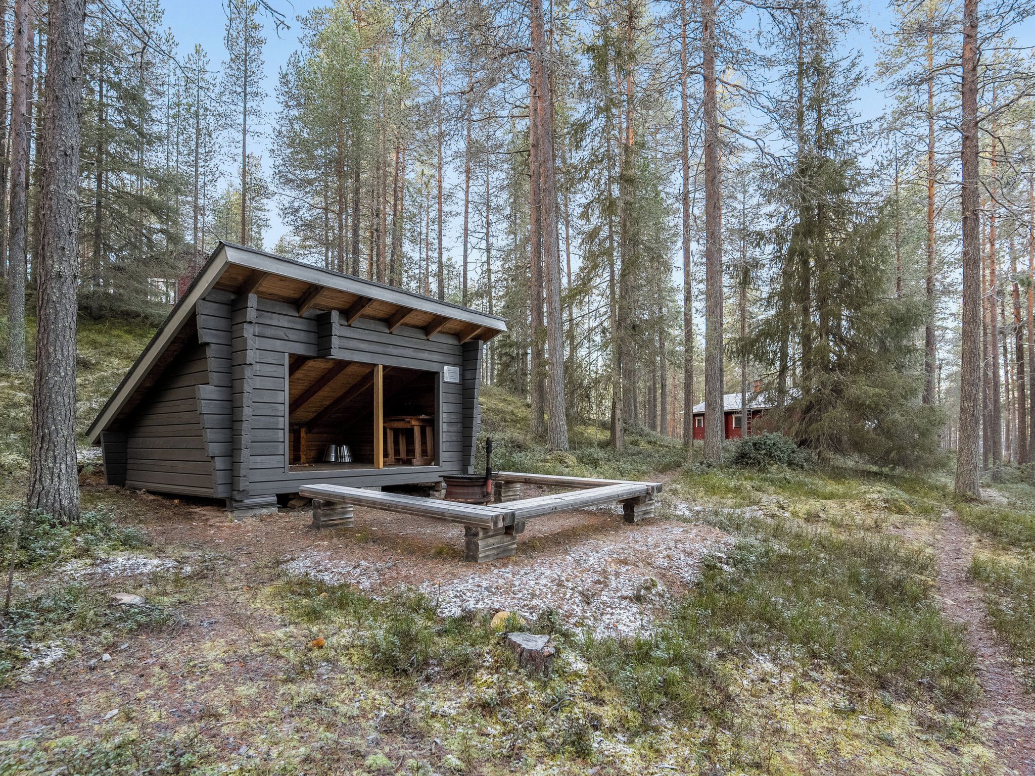 Eine Hütte mit geneigtem Dach, einer Holterrasse und einem Feuerkorb in einem bewaldeten Gebiet.
