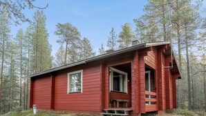 Eine rote Holzhütte mit Veranda, umgeben von einem Wald.