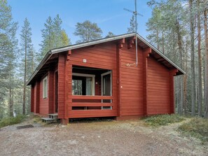 A red cabin with a porch, surrounded by a forest.