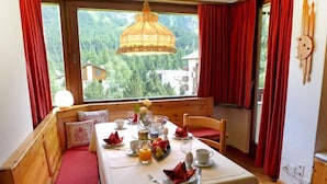A dining area with a table set for two, a bench with cushions, and a view of a forest through large windows.