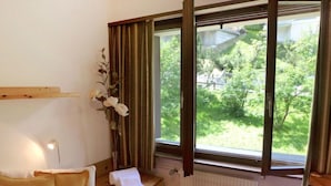 A room with a bed, a wooden nightstand, a radiator, and a window with curtains.