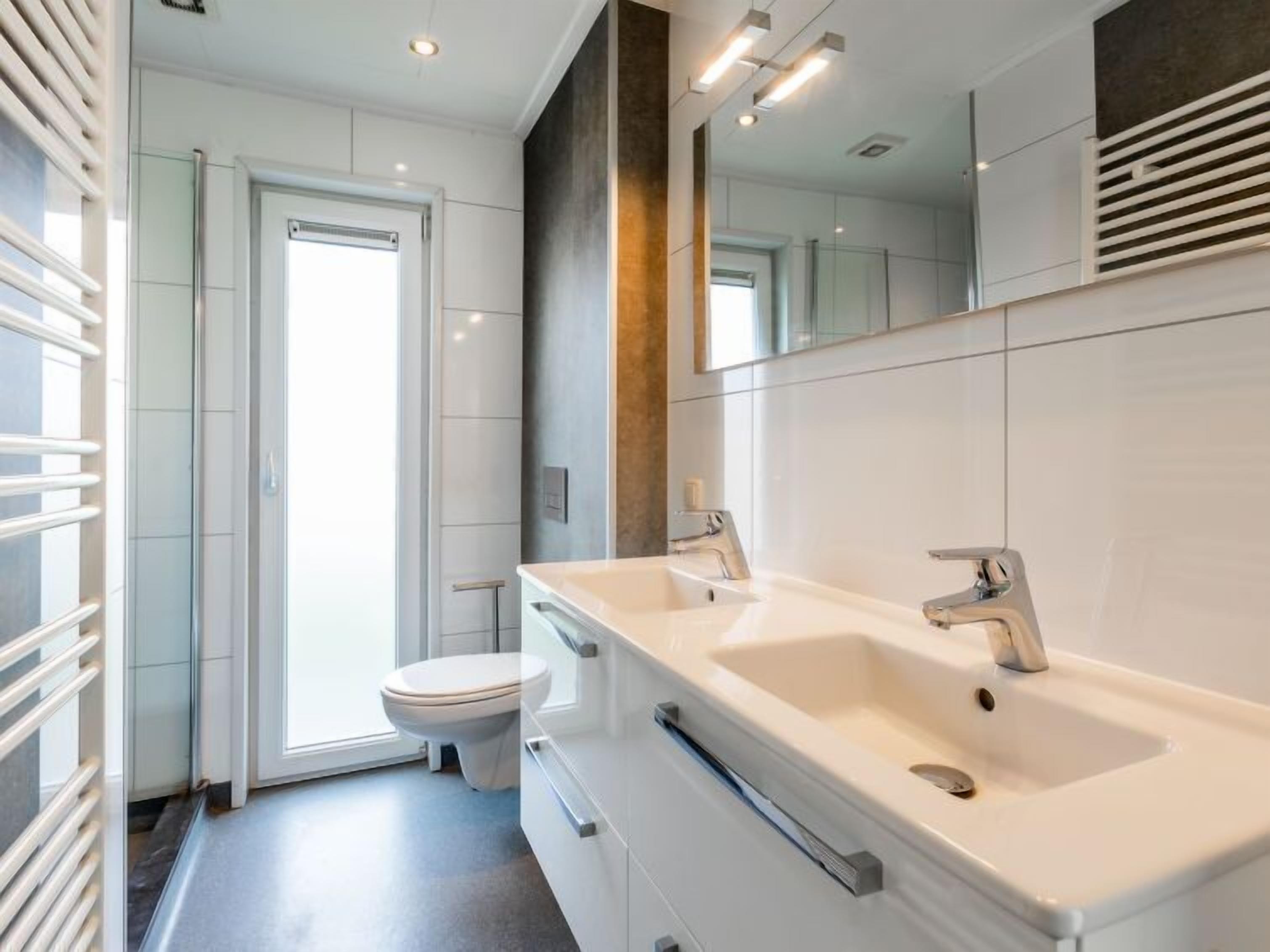 A modern bathroom with a large mirror, a double sink, and a toilet.