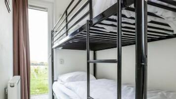 Een slaapkamer met een stapelbed, raam, radiator en deur.