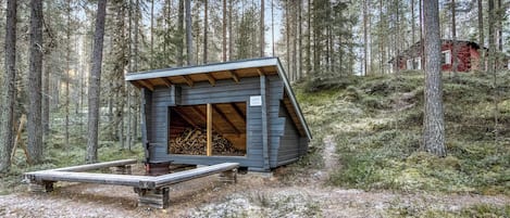Una cabaña con techo inclinado, terraza de madera y una zona para hacer fuego.