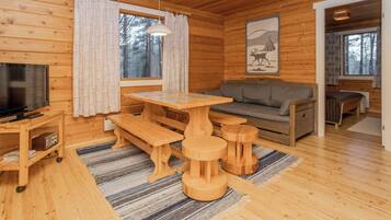 Interior de una cabaña de madera con televisión, un sofá, una mesa de comedor y un banco.