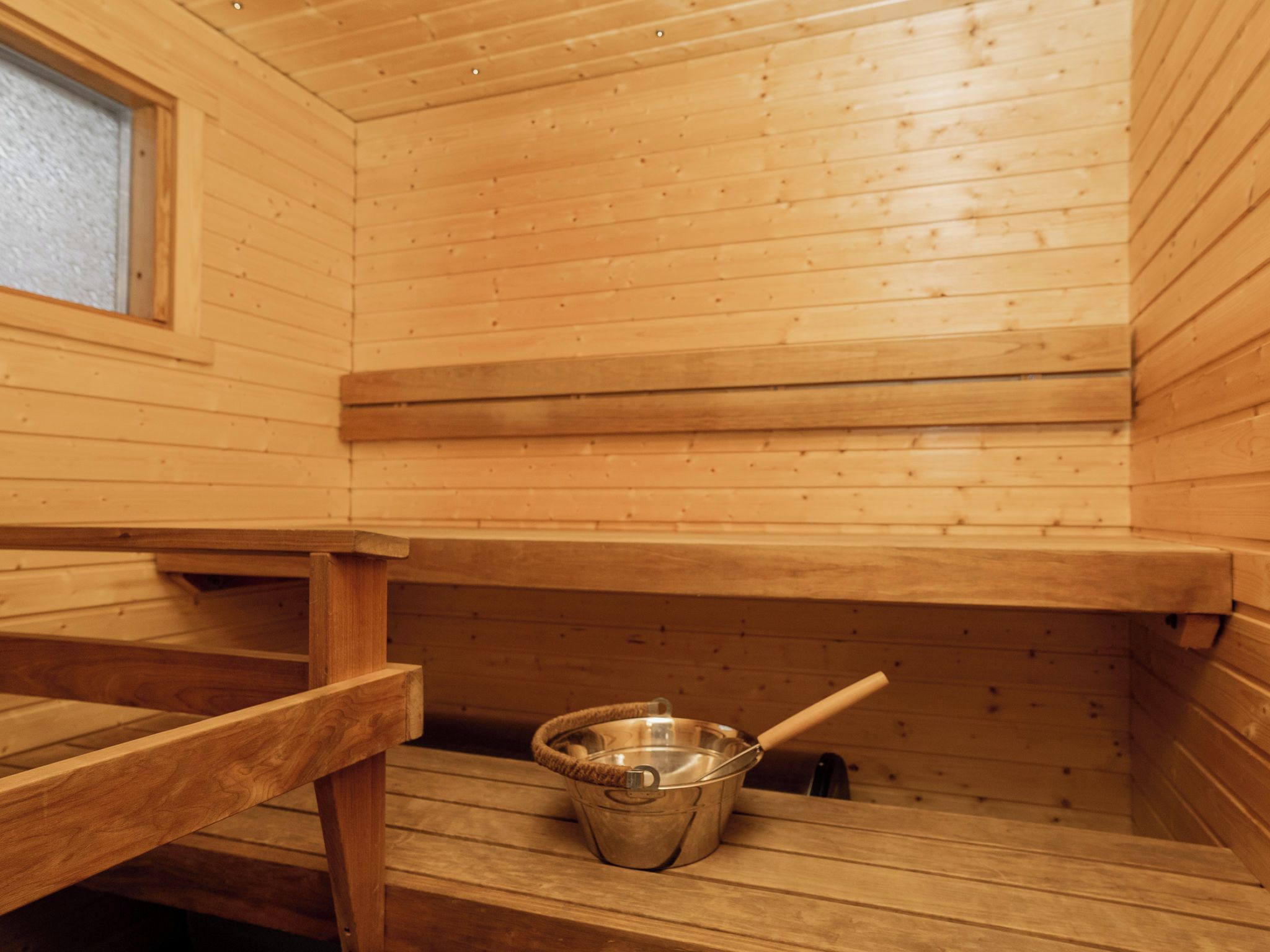 Uma sala de sauna com bancos de madeira e um balde de metal.