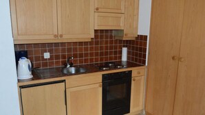 A compact kitchen with wooden cabinets, a stainless steel sink, a black dishwasher, and a tiled backsplash.