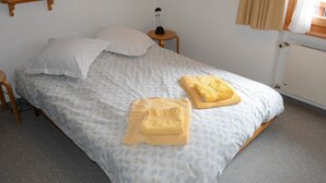 A single bed with a patterned bedspread, two pillows, a bedside table with a lamp, and a window with curtains.