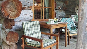 A rustic cabin interior with a wooden table, a plaid chair, and a bench with a patterned cushion. - Alppimaja by Interhome (Asikkala)