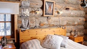A rustic log cabin bedroom with a wooden bed, two bedside tables, and a window with curtains. - Alppimaja by Interhome (Asikkala)