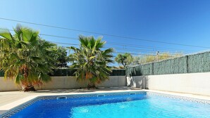 Une piscine dont le fond est recouvert de carreaux disposés selon un motif géométrique, entourée d’un petit muret et de palmiers.