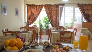 A dining area with a table set for breakfast, including fruits, eggs, bread, and beverages. - Dorana Trekking Hotel (Karpathos)