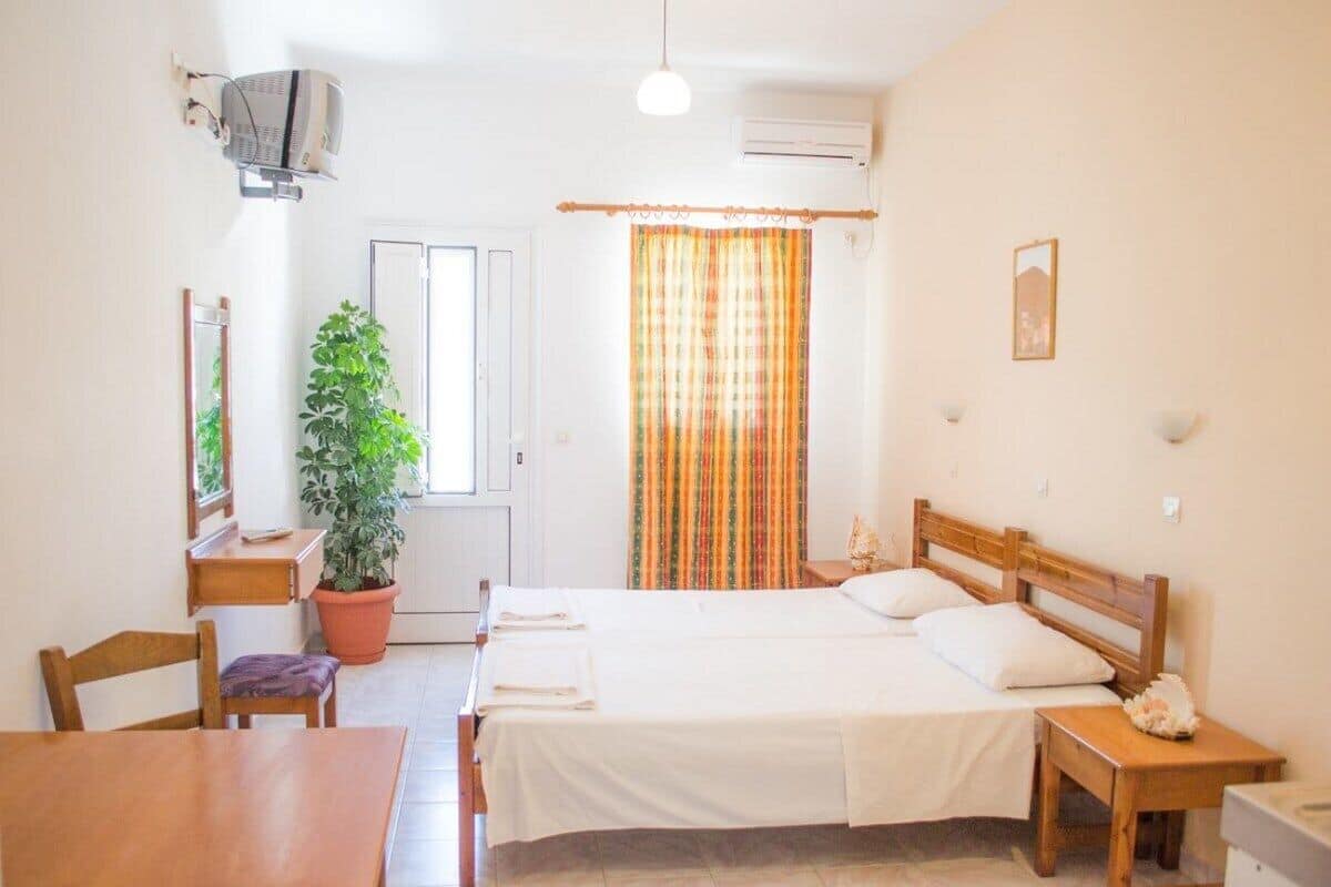 Ein Schlafzimmer mit einem Bett, Nachttischen, einem Sessel, einer Topfpflanze und einem Fenster mit Vorhängen.