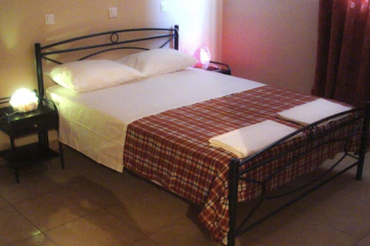 Ein Einzelbett mit Metallgestell, einer weißen Bettdecke und einer karierten Decke. Es gibt zwei Nachttische mit Lampen.