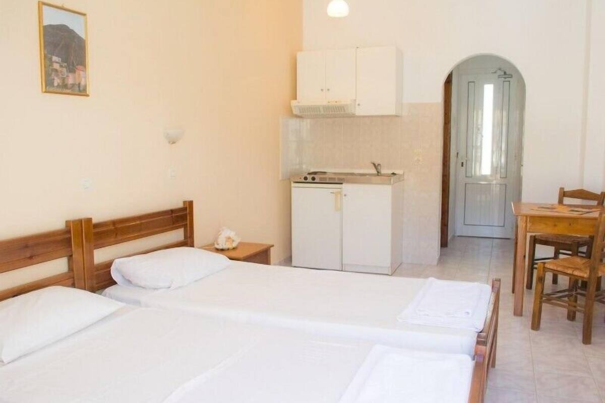 Ein Zimmer mit zwei Betten, einer kleinen Küchenzeile und einem Essbereich.