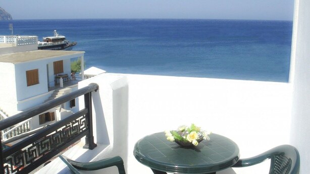 A balcony with a table and chairs, overlooking a clear blue sea and a distant island. - Dorana Trekking Hotel (Karpathos)