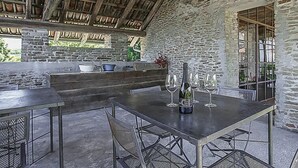 Un patio al aire libre con paredes de piedra, vigas de madera y una mesa con copas de vino y una botella.