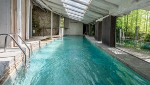 Una piscina interior con tragaluces, una pared de piedra y un cerramiento de cristal para ver el exterior.