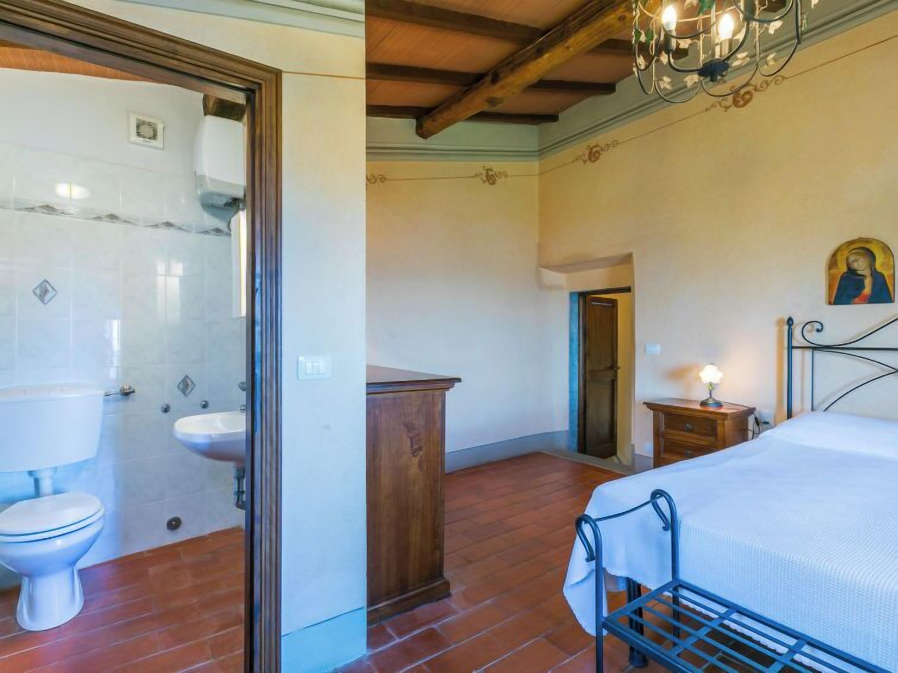 Une pièce comprenant un lit, une armoire en bois, une table de chevet avec une lampe et une porte donnant sur une autre pièce.