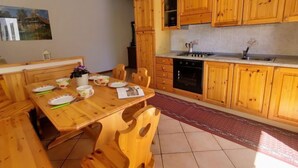 Un tavolo da pranzo in legno con sedie, una cucina con mobili in legno, un fornello e un lavello.