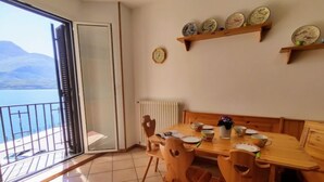 Zona pranzo con tavolo e sedie, vista sul mare, una sveglia e un ripiano con piatti.