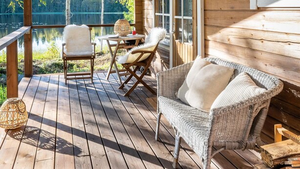 A wooden deck with wicker furniture, a table, and chairs overlooking a lake. - Niemenkärki, vaikon loma 8 by Interhome (Kaavi)