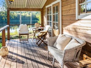 Una terraza de madera con mobiliario de mimbre, una mesa y sillas con vistas a un lago.