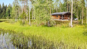 A cabin surrounded by a forest with a pond in the foreground. - Niemenkärki, vaikon loma 8 by Interhome (Kaavi)