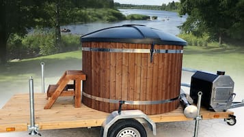Kannettava sauna, jossa on puinen ulkokuori, metallirunko ja siihen kiinnitetty grilli.