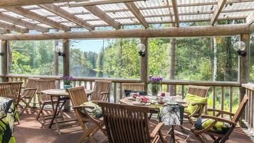A covered outdoor seating area with wooden furniture and a table set for dining.