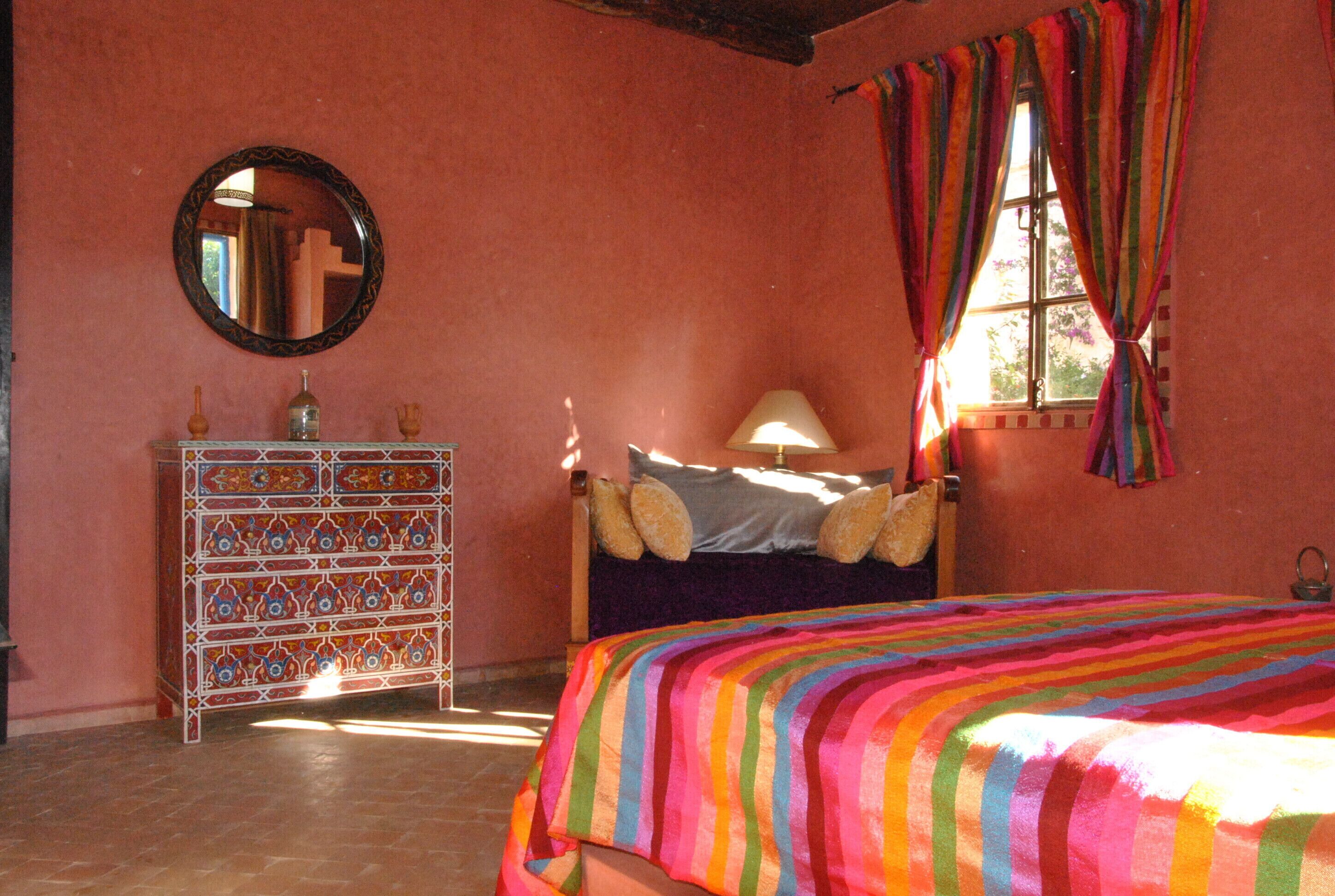 A bedroom with a bed, a dresser, a mirror, and a window with curtains.