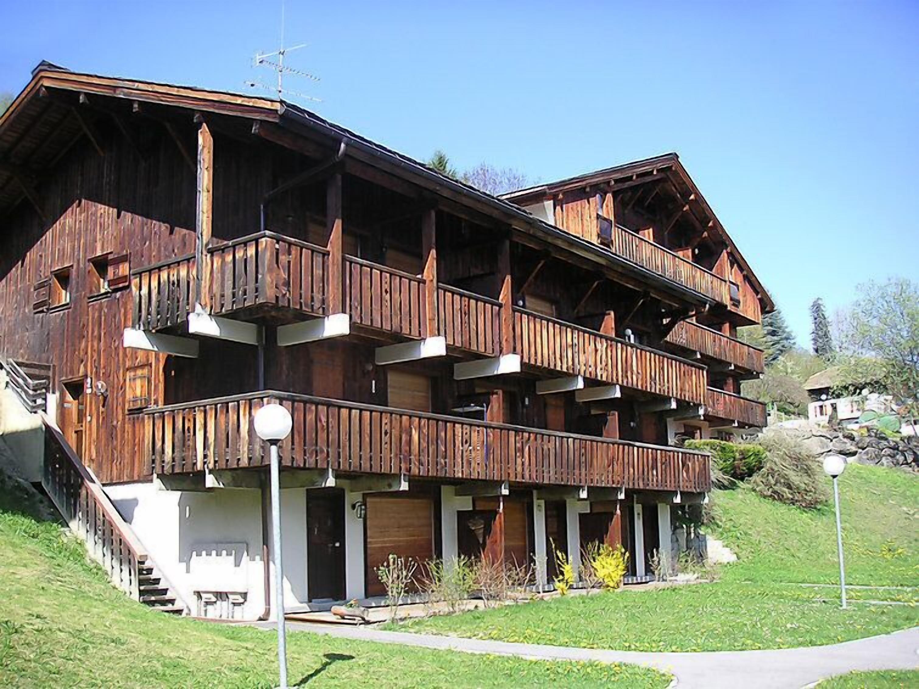Una cabaña de madera de varios pisos con balcones, una escalera y un césped cuidado.