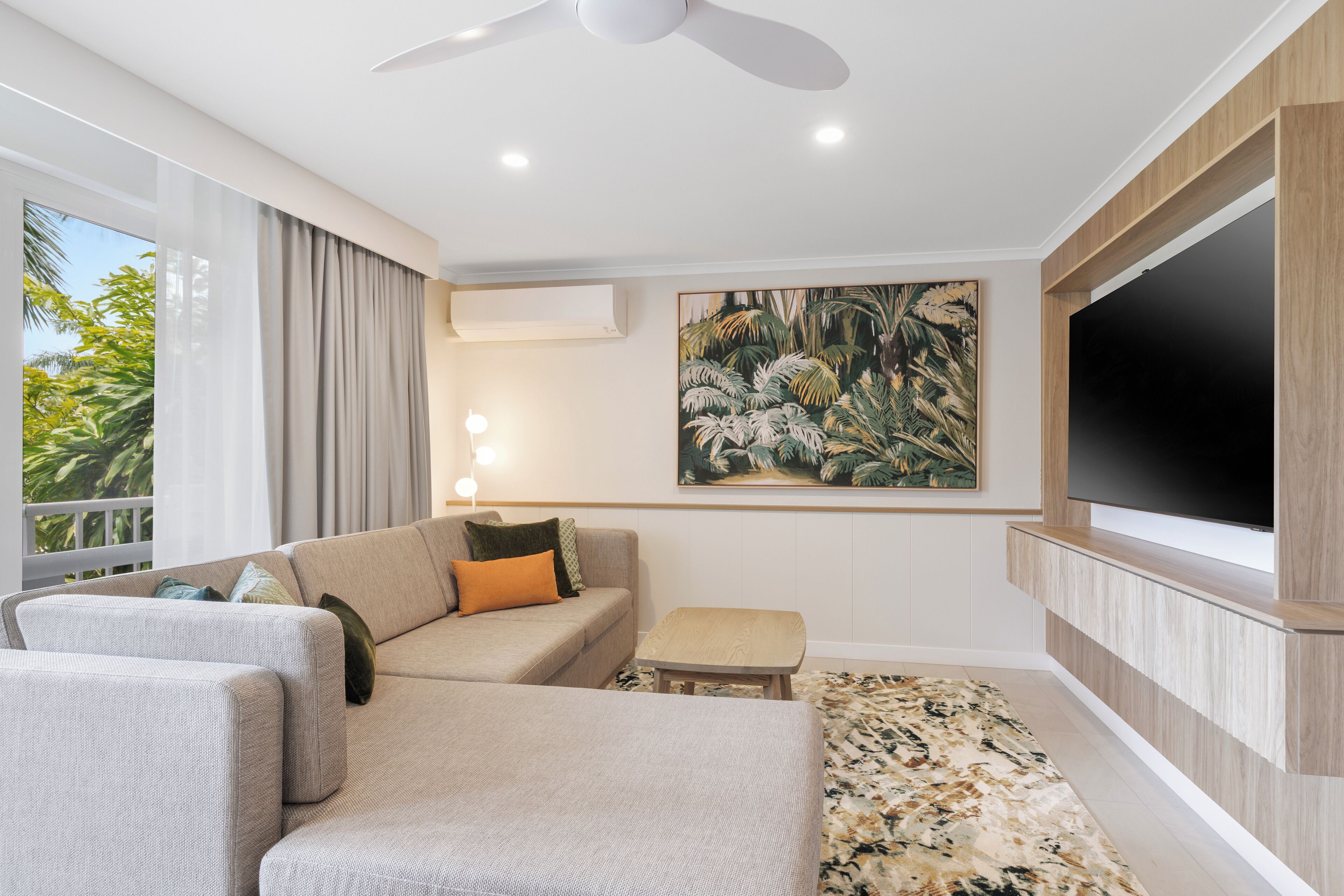 A modern hotel room with a sofa, a small table, a painting, and a TV mounted on the wall.