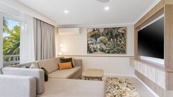 A modern hotel room with a sofa, a small table, a painting, and a TV mounted on the wall.