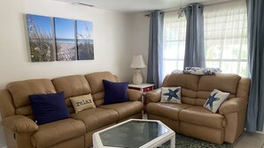 A living room with two brown leather sofas, a glass coffee table, and a patterned rug. There are two wall-mounted paintings and a lamp on a side table. - Great location! Private fenced backyard. March/April 2027 available (Englewood)