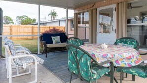 A covered patio area with a table and chairs, a cushioned bench, and a view of a backyard. - Great location! Private fenced backyard. March/April 2027 available (Englewood)