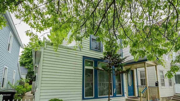 A two-story house with a front porch, a small tree, and a white picket fence.
