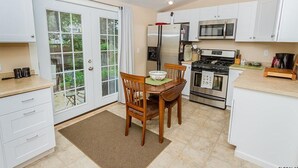 A kitchen with white cabinets, a stainless steel refrigerator, a microwave, and a stove. There is a dining table with chairs and a window with curtains.