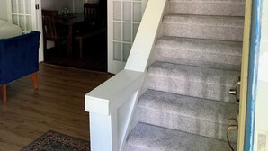 A staircase with a white handrail leading to a second floor. A blue chair and a patterned rug are visible in the foreground.
