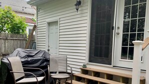A wooden deck with a covered grill, a chair, and a small table.