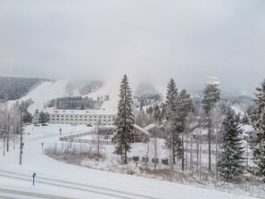 Un paysage enneigé avec un bâtiment qui semble être un hôtel ou un complexe touristique, entouré d’arbres et avec une piste de ski en arrière-plan.