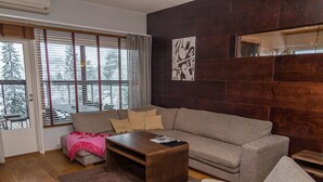 Een moderne woonkamer met een bank, een salontafel en een stoel. Er is een raam met zonwering, een open haard en een wanddecoratie.