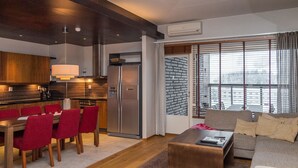 Een moderne woonkamer met een bank, een salontafel en een eethoek met rode stoelen. Er is een keuken met donkerhouten kastjes en een roestvrijstalen koelkast.