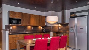 Een moderne keuken met houten kastjes, een roestvrijstalen koelkast en een eettafel met rode stoelen.